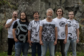 Kuusi miestä seisoo ruohikolla kuviollisissa t-paidoissa, joka paidassa on erilainen kuviointi