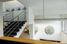 Indoor staircase at K1 building on the left, Anssi Kasitonni's artwork Polaris (2023) on the upstairs on a white wall. On the right side of the image is Anssi Laitinen's artwork Willow Wiew (2023).