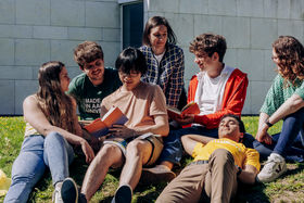 A group of students sitting outside on grass and reading.