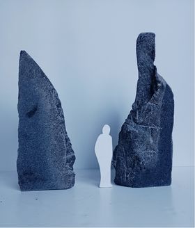 A proposal image of a sculpture made of two upward spiking granite pieces, with a white cardboard person depicting human scale in the middle of the two pieces.