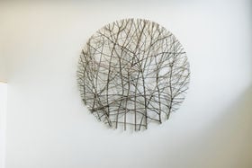 A round sculpture made of willow tree hangs on a white wall.