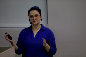 A presenter speaks at the front of a lecture hall.