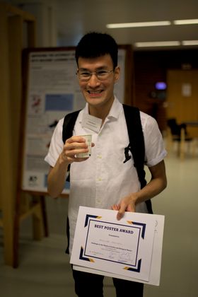 An attendee stands with a sheet of paper upon which is written "best poster award."