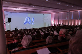 Kuvattu takaapäin salista niin, että näkyy yleisö ja valkokankaalla Aalto Day Onen visuaalinen ilme.