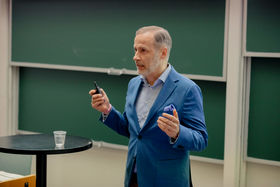 A man in a blue blazer speaking and holding a clicker in his hand