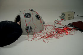 A person laying down, their head inside a dome like speaker surrounded by red cables