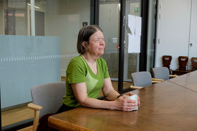 A woman with a green t shirt sitting at the table holding an item while her eyes are closed
