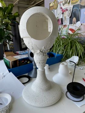 A white concrete artefact standing on a table full of prototypes and clutter