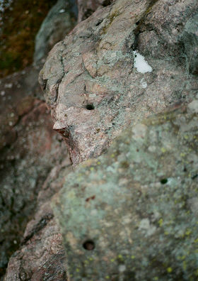 A large rock in nature with a pink greenish tint and an occasional hole in it