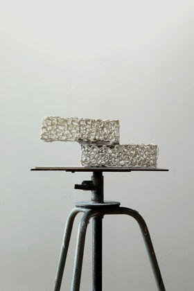 Two fragile looking ceramic objects that look like bricks presented on a stool