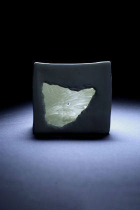 A cube shaped ceramic object with a hole in it, in the hole there is a crystal like texture and light is coming out of it