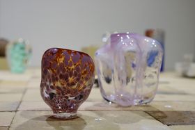 On the left is a patchy red-orange-violet glass sculpture and on the right a clear-pink one