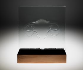 A transparent glass sheet, on it an outline of a uterus. The glass is inserted into a block of wood