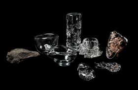 A collection of colourless glass objects and two large stones against a black background 