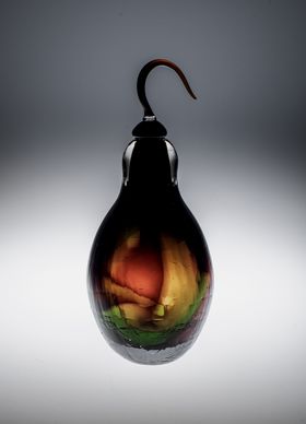Dark bulbous pear-shaped glass object with orange, yellow and green colours shimmering in it 