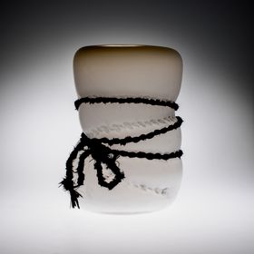 A black rope squeezing a white-beige glass sculpture 