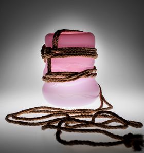 A brown rope wrapped and tied around a pink glass sculpture 