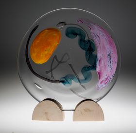 A circular, cell-like glass object with colourful shapes inside it