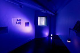 A room fully lit up by a blue purple-light directed towards some prints presented on the wall
