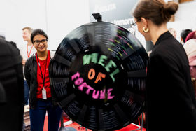 A person is standing next to a wheel of fortune that another person is rolling