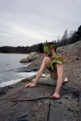 A man sitting on the beach dressed in a costume made of algae
