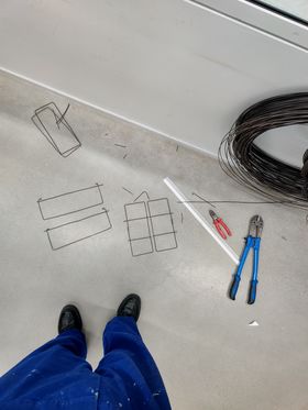 In the workshop, making a wire frame while dressed in blue overalls 