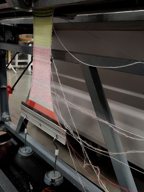 A machine weaving a spread of pink-green textile