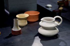 A collection of ceramic objects, a white vessel with a handle and a spout in the forefront
