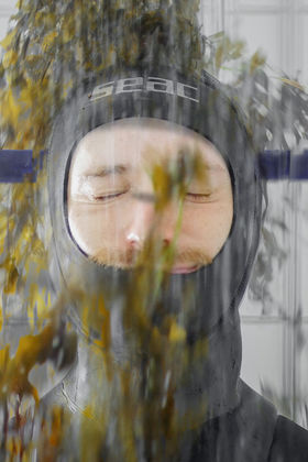 A person being showered by algae while wearing a full body neoprene suit