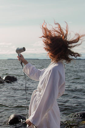 A person drying their hair with an electric fan on the beach