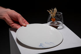 A hand picking up a ceramic plate, next to it is a glass shaped by the rock it rests upon