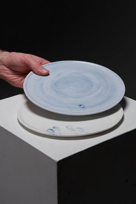 Two ceramic plates - one white with a blue trace of a hand and the other light blue with a hand picking it up