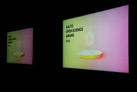 Two screens with a yellow and pink gradient, a yellow ball hovering over a podium and the text Aalto Open Science Award 2023.