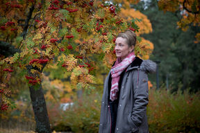 Johanna Kaipio seisoo ulkona, taustalla ruskan värittämä pihlajapuu ja pensaita.