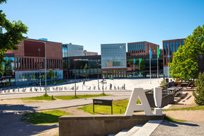 White Aalto logo with exclamation mark standing in the middle of Otaniemi campus in the summertime