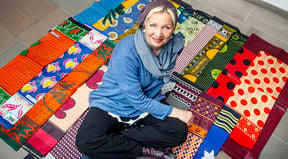 Saija Hollmén istumassa lattialla risti-istunnassa värikkäiden afrikkalaisten kankaiden päällä.