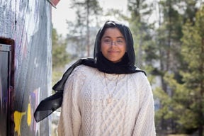 Afrin Hossain stood by a wall with trees in the background