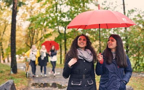 Two women walking in the campus area and carrying an Aalto umbrella