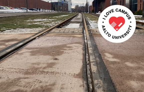 Tram tracks on campus, some snow on the ground, with red-bricked buildings on both sides of the tracks