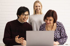 Kolme ihmistä katsoo jotain kannettavan tietokoneen näytöltä hymyillen.