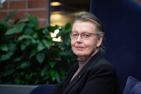 Professori Kaisa Nyberg istuu isolla tuolilla Aalto-yliopiston tietotekniikan talossa, tasutalla on viherkasveja