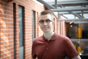 Associate Professor Jukka Suomela smiling at camera, dressed in a red shirt against a red-brick wall at the Department of Computer Science