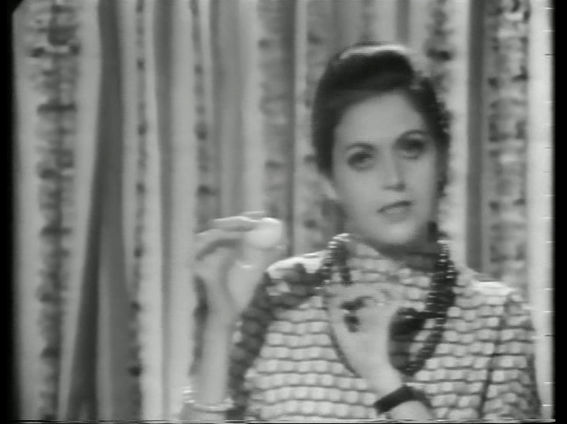 Video still from SALIMA HASHMI, Hunda Hubalna (how to boil an egg), 1970. The artist is featured holding an egg. Black and white image.