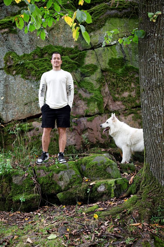 Henkilökuvassa Kalle Järvenpää seisoo sammaloituneen kiven päällä suuren puun alla ja hänen vieressään on valkoinen koira.