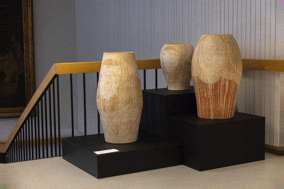 Three reddish ceramic pots sit on individual pedestals near a staircase in a lobby area