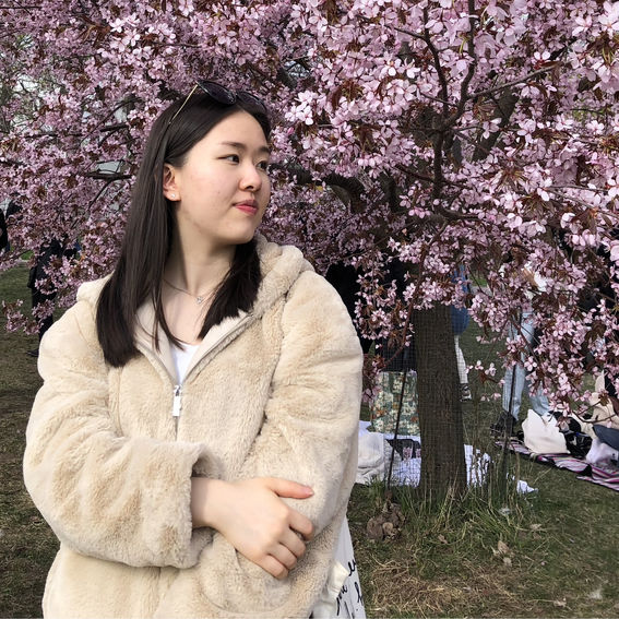 Kuvassa näkyy Anni Zhao kukkivan vaalenanpunaisen kirsikkapuun edessä. 