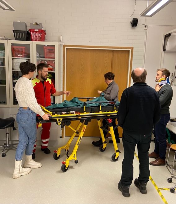 Two team members discuss with three paramedics, around stretchers in the emergency simulations lab