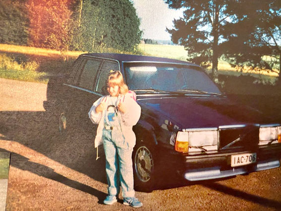 Kuvassa nuori Satu Rämö seisoo ulkona auton edessä.  