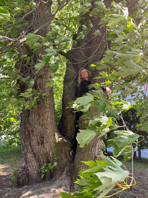 Professori Ranja Hautamäki halaa hymyillen suurta puuta 