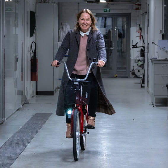 Professor Tiina Nypelö smiling and riding a red bicycle inside of a research facility
